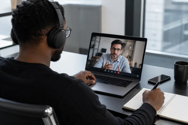 Un consultant prend des notes pendant un échange vidéo sur son ordinateur portable.
